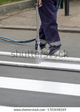 Details with a road worker painting a crosswalk on a city street.