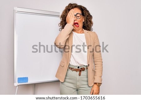 Middle age senior business woman standing on seminar presentation by magnectic blackboard Yawning tired covering half face, eye and mouth with hand. Face hurts in pain.