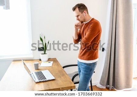 The guy uses a laptop to work. Concentrated guy looks on the screen with a serious face and thinks about something, looking for a solution to tasks. Remote work