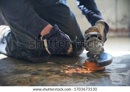A man in gloves and protective knee pads on the legs grinds the floor with a grinder