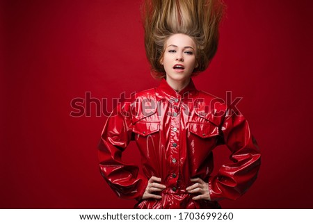 Cheerful woman with fair hair on top in red suit rejoices, picture isolated on red background