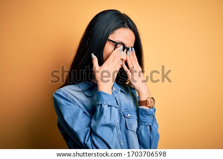 Young beautiful chinese woman wearing casual denim shirt over isolated yellow background rubbing eyes for fatigue and headache, sleepy and tired expression. Vision problem