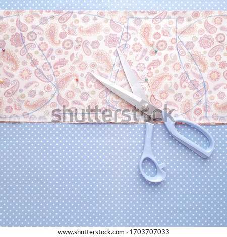 making fabric face mask cutting by 
scissors  put on light blue background cloth 