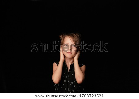 A girl of 6 years, against a dark background. Covers his ears with his hands. I can't hear evil.