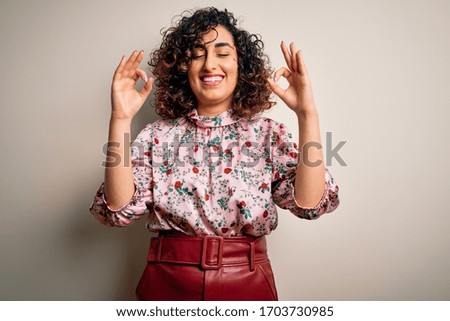 Young beautiful curly arab woman wearing floral t-shirt standing over isolated white background relax and smiling with eyes closed doing meditation gesture with fingers. Yoga concept.