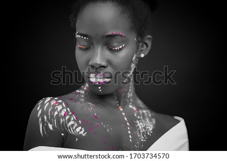 african woman with body art glowing in ultraviolet light. Portrait of beautiful woman painted in fluorescent powder. isolated dark space. black and white photo