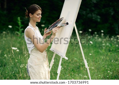 young easel woman paints on a white canvas in the street