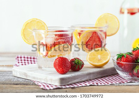 Refreshing homemade lemonade with fresh strawberry, lemon and ice. Healthy cold drink, low calories. Tasty cool summer beverage. Wooden white background, two glasses