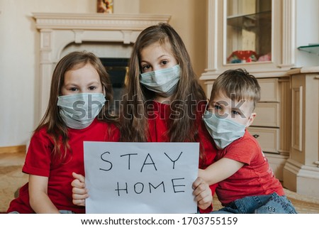 Family stay at home concept. Three children in mask holding sign saying stay at home for virus protection and take care of their health from COVID-19. Quarantine concept.