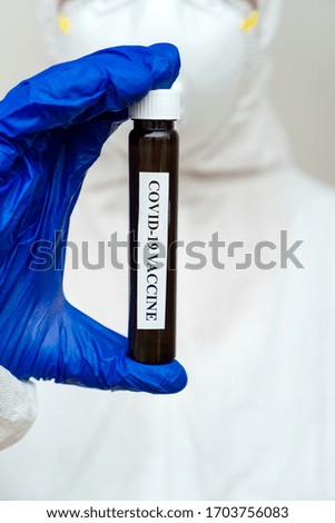 Human in biohazard suit holding Coronavirus Vaccine.