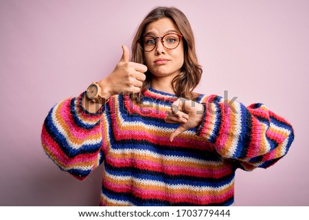 Young beautiful blonde girl wearing glasses and casual sweater over pink isolated background Doing thumbs up and down, disagreement and agreement expression. Crazy conflict