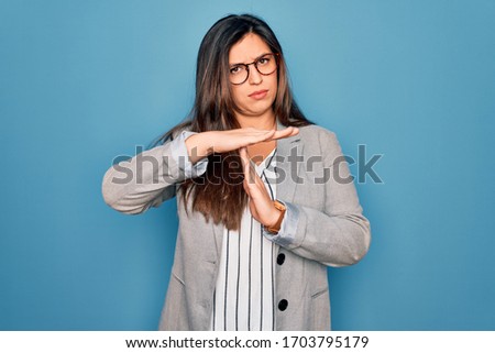 Young hispanic business woman wearing glasses standing over blue isolated background Doing time out gesture with hands, frustrated and serious face