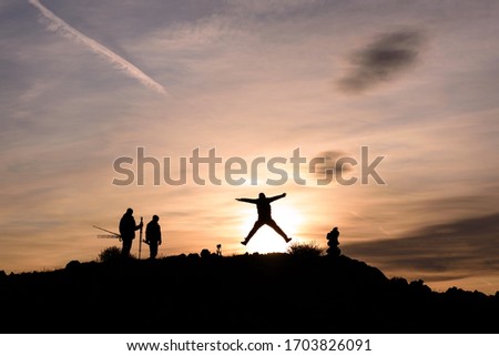 Silhouettes of people on the side of a mountain in the sunlight at sunrise against a blue sky with clouds