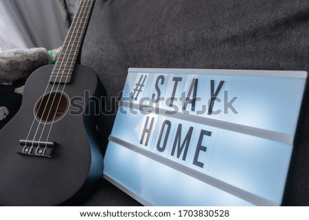 Coronavirus home lightbox sign with hashtag message #STAYHOME glowing on home sofa with cozy. COVID-19 text to promote self isolation staying at home.