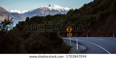 Beautiful panorama of the road towards Glenorchy with a traffic sign in the foreground and the snowy mountain in the background taken on a winter day in Queenstown, New Zealand