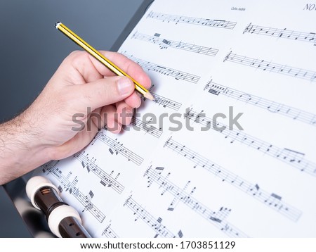 hands of a man writing a musical score or musical sheet, flute or recorder shown, musical composition concept Royalty-Free Stock Photo #1703851129