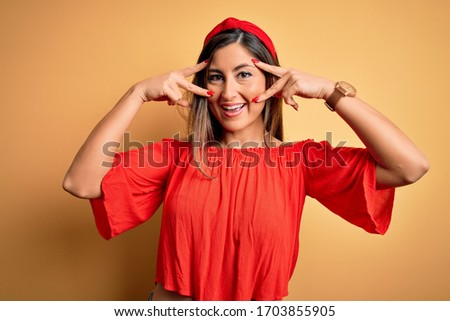 Young beautiful woman colorful summer style over yellow isolated background Doing peace symbol with fingers over face, smiling cheerful showing victory