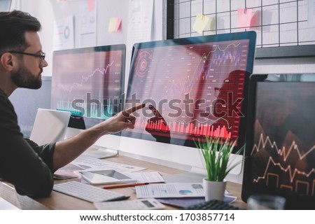 Side view of data analyst pointing with finger at charts on computer monitor while testing protection of computer systems