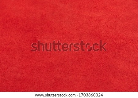 Red matte background of suede fabric, closeup. Velvet texture of seamless leather. Felt material macro. Red suede texture. Fabric, leather, material for designers.