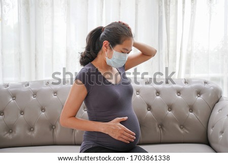 A pregnant woman wears a surgical mask is feeling unwell and sick on the sofa. to protect a COVID-19 (Coronavirus), PM 2.5 and prevent infection to the fetus concept. Royalty-Free Stock Photo #1703861338