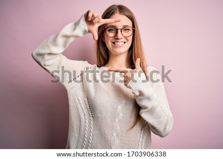 Young beautiful redhead woman wearing casual sweater and glasses over pink background smiling making frame with hands and fingers with happy face. Creativity and photography concept.