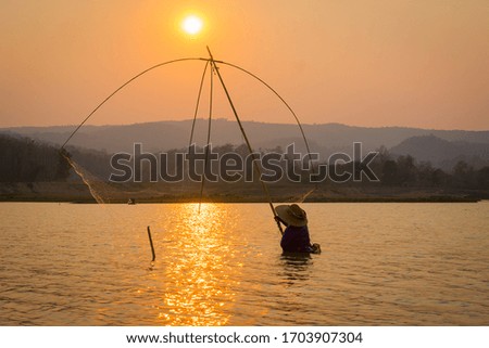 Asian fisherman on silhouette sunrise with gear fishing on the lake 