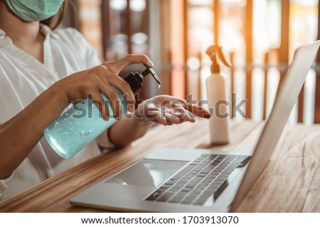 Office worker working from home during coronavirus outbreak cleaning her hands with sanitizer gel and wearing protective mask. Coronavirus, covid-19, Work from home (WFH), Social distancing concept. Royalty-Free Stock Photo #1703913070