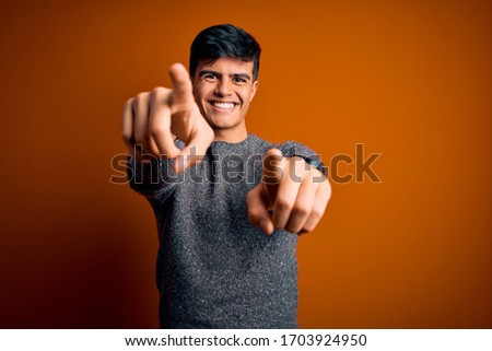 Young handsome man wearing casual sweater standing over isolated orange background pointing to you and the camera with fingers, smiling positive and cheerful