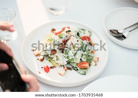 Fresh and Delicious Caesar Salad on White Dish with People Take a Picture as Foreground