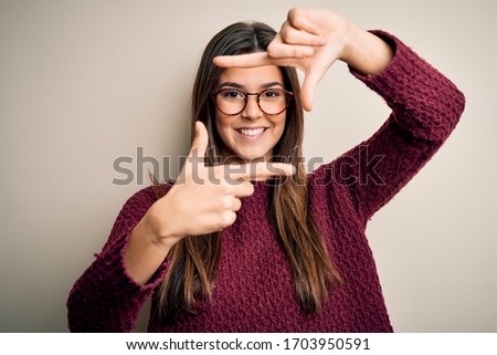 Young beautiful girl wearing casual sweater and glasses over isolated white background smiling making frame with hands and fingers with happy face. Creativity and photography concept.