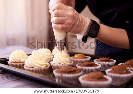 Chocolate cupcakes with a swirl of cream.Female hands fill cupcakes on a baking sheet. Royalty-Free Stock Photo #1703951179