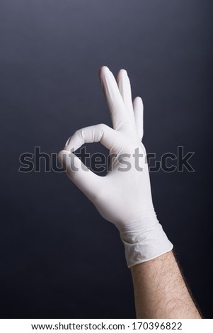Male hand in latex glove showing OK sign on dark background