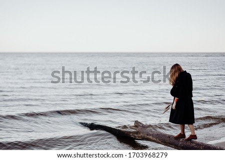 A girl in a black dress and white shirt walks along a deserted sea shore in calm weather and completely calm. Minimalism