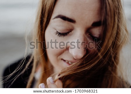 portrait of a sad girl on the ocean in a black dress and her hair developing in the wind and waves rolling on the birch with dry grass in her hands. blurred background