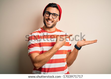Young handsome man wearing casual striped t-shirt and glasses over white background amazed and smiling to the camera while presenting with hand and pointing with finger.
