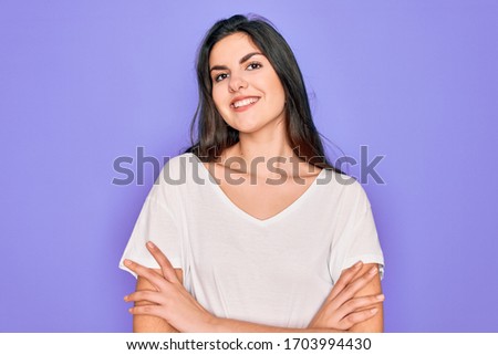 Young beautiful brunette woman wearing casual white t-shirt over purple background happy face smiling with crossed arms looking at the camera. Positive person.
