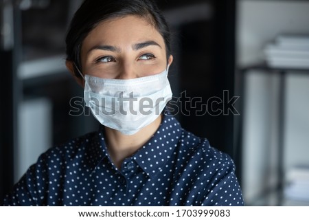 Hopeful smiling young woman in protective face mask look in distance hope for coronavirus pandemic end, happy millennial female in medical facial cover from COVID-19 thinking, healthcare concept Royalty-Free Stock Photo #1703999083