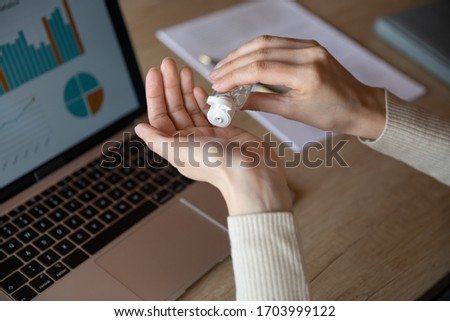Close up of woman worker sit in office cleanse hands with sanitizer take care of health during coronavirus pandemic, female employee use antibacterial liquid at workplace against covid-19 outbreak Royalty-Free Stock Photo #1703999122