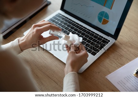 Close up top view of female worker cleanse laptop in office with antibacterial liquid, woman employee disinfect computer and workplace with sanitizer, take measures during coronavirus pandemic Royalty-Free Stock Photo #1703999212