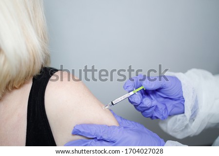 Microbiologist or medical worker with blue surgical gloves giving the vaccine with a syringe for the rapidly spreading Coronavirus to a old women. COVID-19 vaccine concept