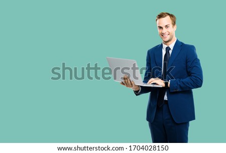Happy smiling business man in blue confident suit, working with laptop, isolated over green marine background. Handsome young man at studio concept picture. Copy space.