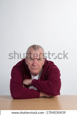 Mature male in studio. bored or worried expression, casual dress with table.