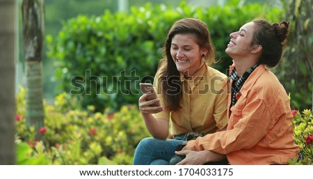 
Female friends taking selfie with cellphone device. Girlfriends taking photo with smartphone outdoors