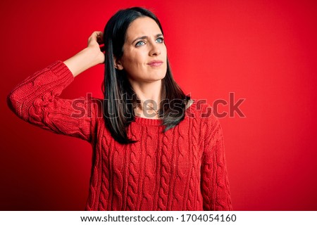 Young brunette woman with blue eyes wearing casual sweater over isolated red background confuse and wondering about question. Uncertain with doubt, thinking with hand on head. Pensive concept.