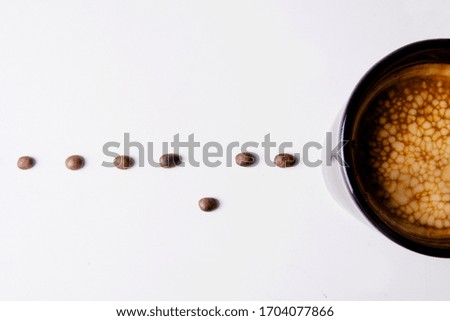 
minimalist composition, black cup of coffee on white background. With path of coffee beans arranged arithmetically