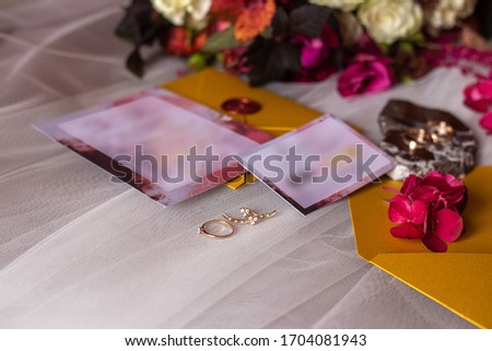 wedding accessories: a bride’s bouquet of roses, peonies and hydrangeas, wedding rings on a stone, a ring and earrings with diamonds, women's shoes, invitation and yellow envelopes with a red wax seal