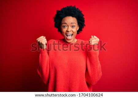 Young beautiful African American afro woman with curly hair wearing casual sweater celebrating surprised and amazed for success with arms raised and open eyes. Winner concept.