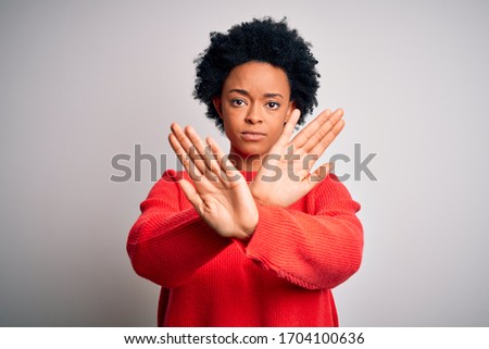 Young beautiful African American afro woman with curly hair wearing red casual sweater Rejection expression crossing arms and palms doing negative sign, angry face