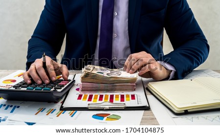 young businessman in suit counts hryvnia money and works with charts and documents as net monthly income. The concept of money is salary or corruption. Work in the office. Royalty-Free Stock Photo #1704104875