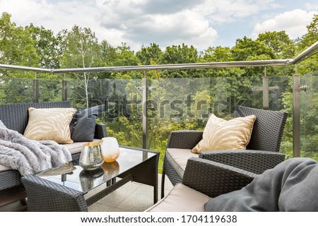Stylish balcony with elegant rattan furniture and glass walls and green forest view Royalty-Free Stock Photo #1704119638